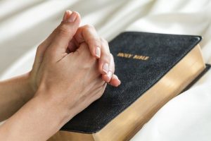 hands praying on a bible